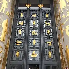 A large metal door is flanked with golden creatures and persons.