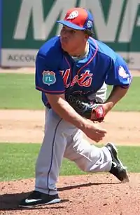 A man in a blue baseball jersey with gray pants and orange cap