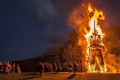 A burning bonfire of a towering 30 foot wickerman holding a sword. A crowd watches from below.