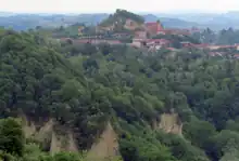 Village with orange roofs are surrounded by rocks and trees.