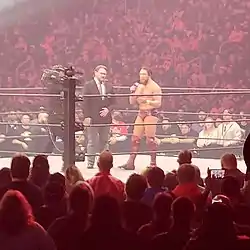 A color photograph of two men and a cameraman in a professional wrestling ring
