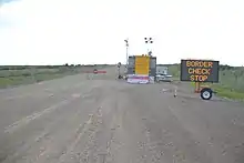 an electronic sign that says "Border Check Stop" on a gravel road.