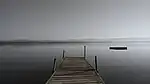 A dock extends from the shore of an extremely wide river.