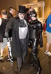 A photograph of cosplayers – a man dressed as the Penguin and a woman dressed as Catwoman