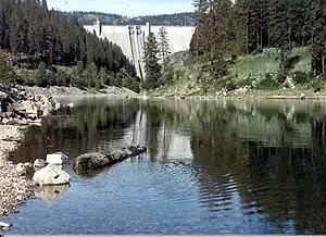 A midsized river flowing through forested hills with a large dam in the distance