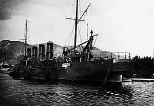 A large gray ship in port, with coal being loaded by a large crane directly behind it.