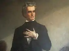 Full profile, black suit with white ruffled shirt. Hand on chest with fingers spread out, soft look.