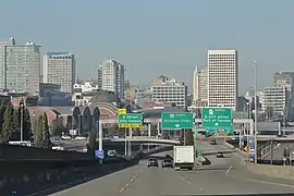 A freeway leading towards a cluster of high-rise buildings, parallel to a railroad