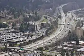 Aerial photograph of a freeway with light traffic passing through a built-up area with car dealerships and office parks