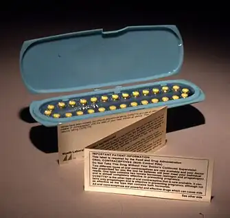 An oblong blue container holding 28 yellow pills, with a small, folded paper note standing in front of it