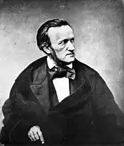 Man wearing a cloak and an outsized bow tie, facing to the right with a severe expression
