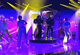 Senhit and Rafal on stage under a disco ball surrounded by backing dancers
