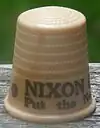 An off-white thimble, with the visible black lettering, "NIXON/Put the ne&nbsp;...