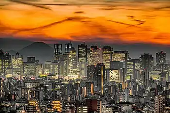 Aerial view of a city; many low-rise buildings in the foreground with many high-rise buildings in the background. The summit of a snow covered mountain can be seen in the distance.