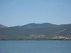 A colour photograph from the middle of a lake of the lake shore with low hills beyond