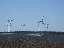 Seven three-blade wind turbines on the shore. A fishing boat is passing by.